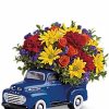 Rustic blue pickup truck container filled with seasonal flowers.