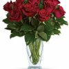Dozen long-stemmed red roses with greenery in a clear vase.