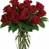 Dozen red roses with greenery in a clear vase.