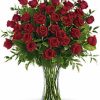 Three dozen long-stemmed red roses in a clear vase with greenery.