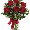 Six red roses with greenery arranged in a clear vase.