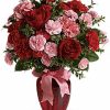 Bouquet of red and pink roses with greenery in a clear vase.