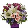 Purple floral arrangement with fresh greenery in a glass vase.