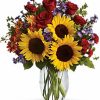 Sunflowers and red roses arranged with greenery in a clear vase.