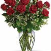 Dozen long-stemmed red roses with greenery in a vase.