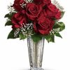 Six red roses with baby’s breath in a clear vase.
