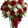Two dozen red and white roses in a tall clear vase with greenery.