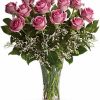 Dozen pink roses with greenery in a vase.