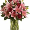 Red roses and pink lilies arranged with greenery in a clear vase.