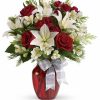 Bouquet of long-stemmed red roses arranged with greenery in a clear vase.